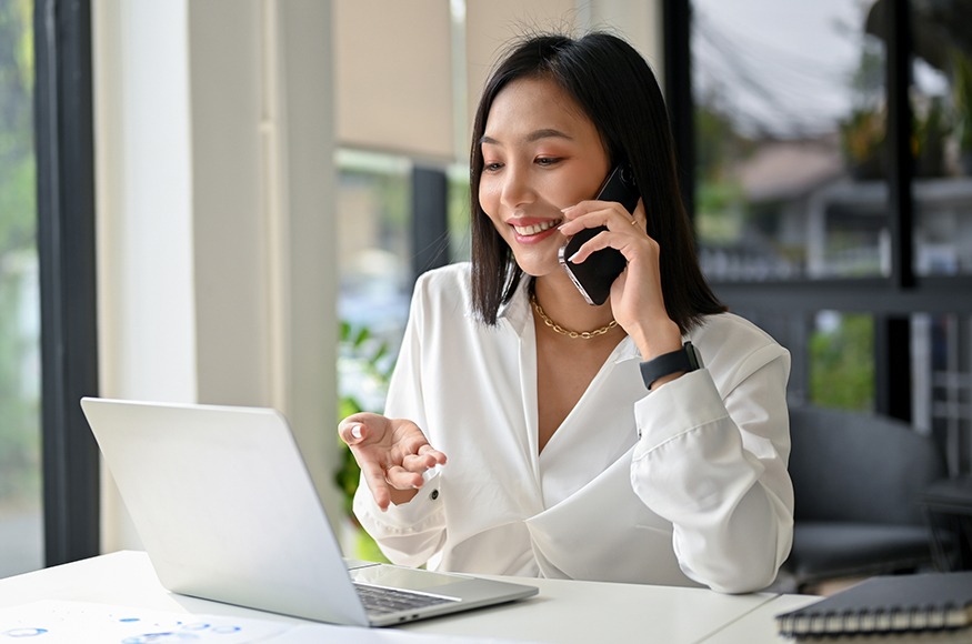 an office lady speaking on the phone and using her laptop